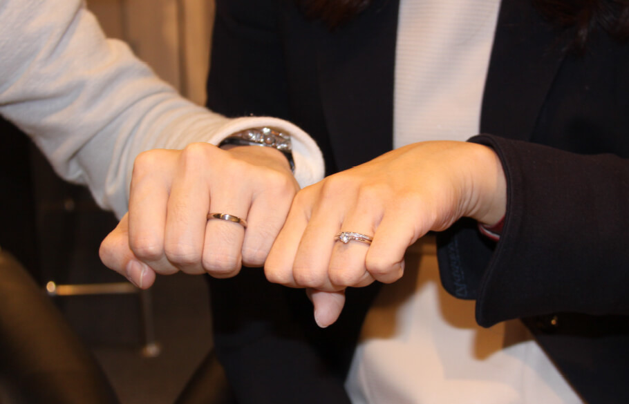 結婚指輪をつけたカップルの手元。女性は婚約指輪と重ね着けしている。