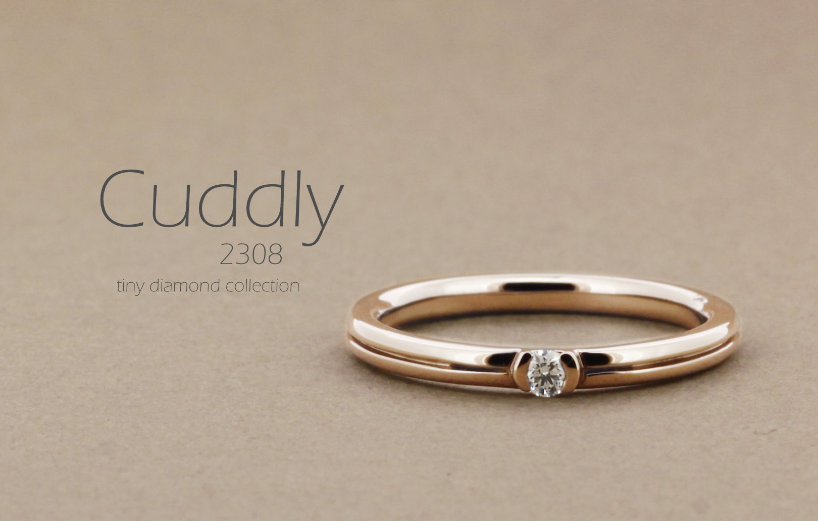 「Cuddly」という名前が付いた、真ん中にラインが入った丸みのあるアームに1粒の小さなダイヤを留めた指輪の詳細ページ