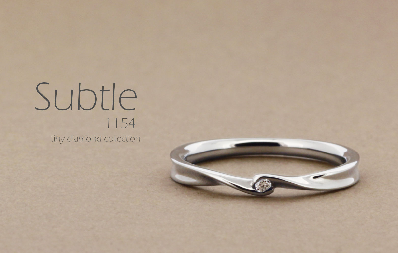 「Subtle」という名前がついた、リボンのようなひねりのあるアームに小さいダイヤを1粒留めた指輪の詳細ページ
